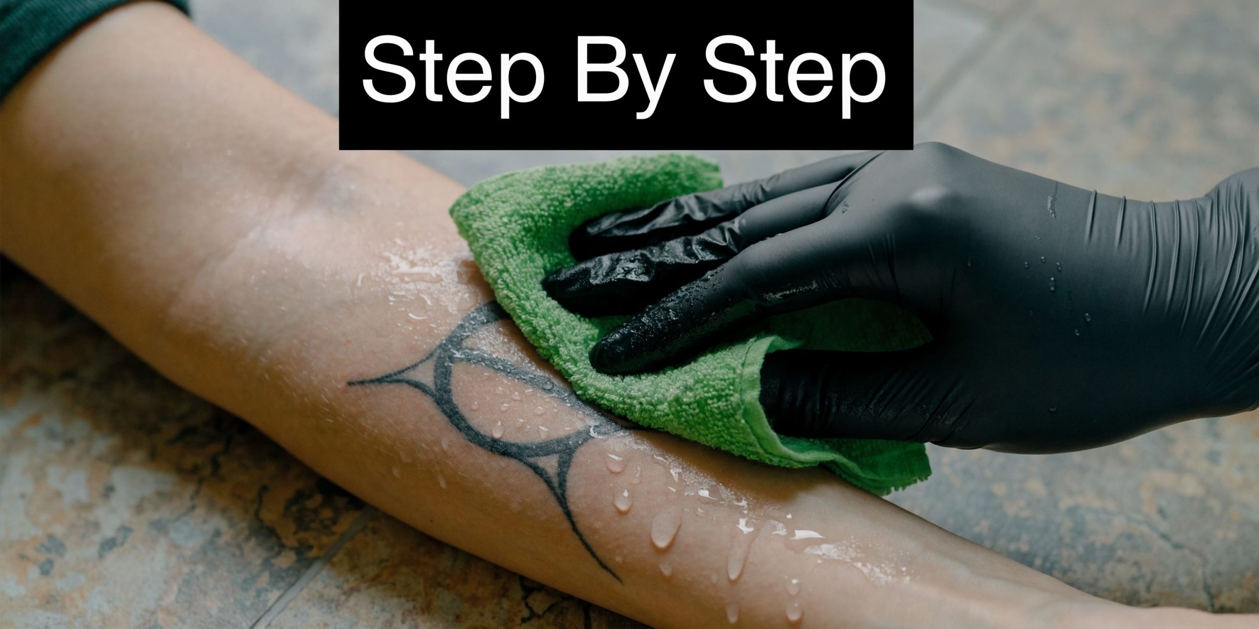 A gloved hand cleaning a healing tattoo on a person's arm with a soft green cloth.