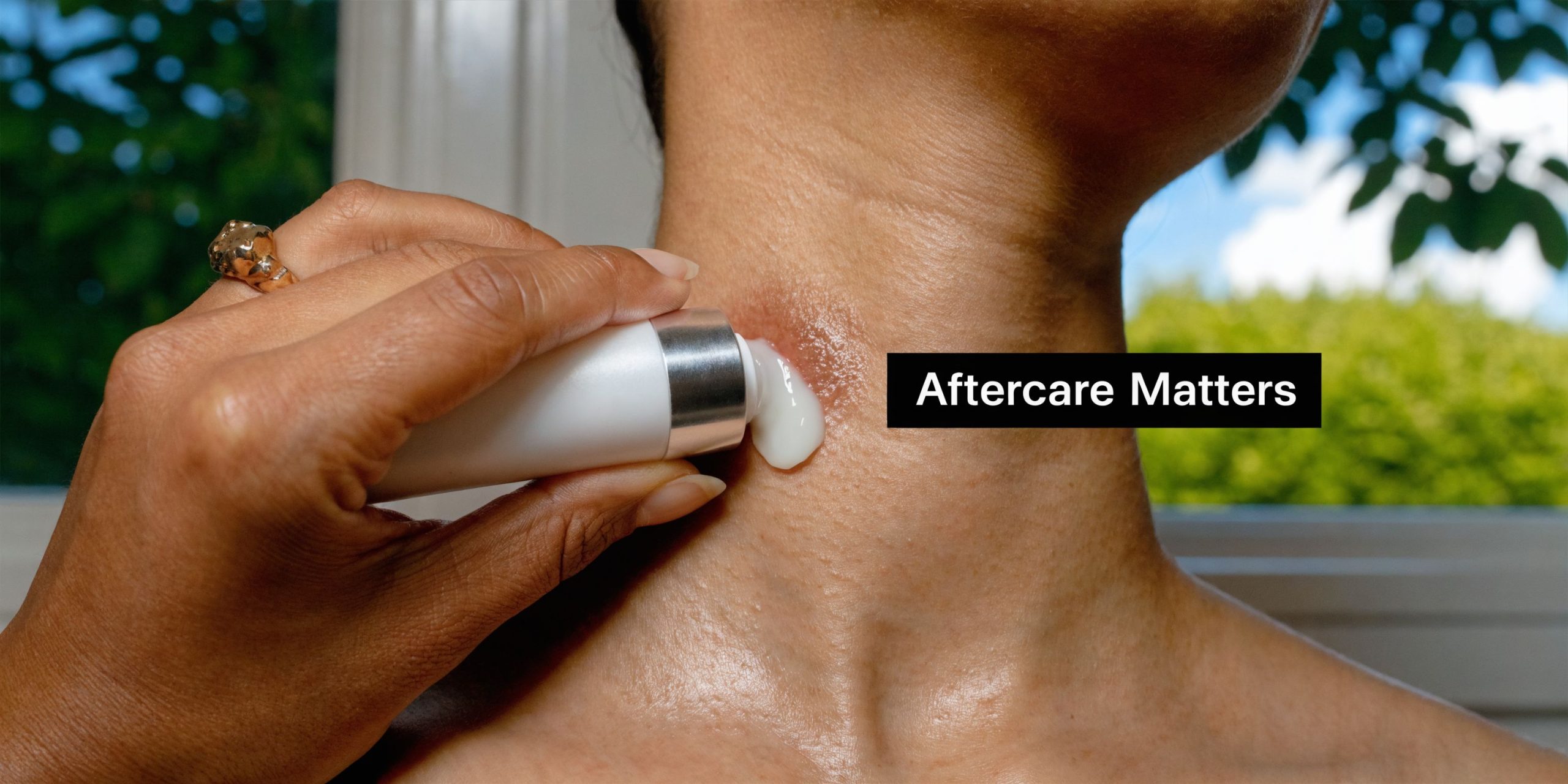 A close-up view of a person applying medicated cream onto a fresh tattoo on their neck.