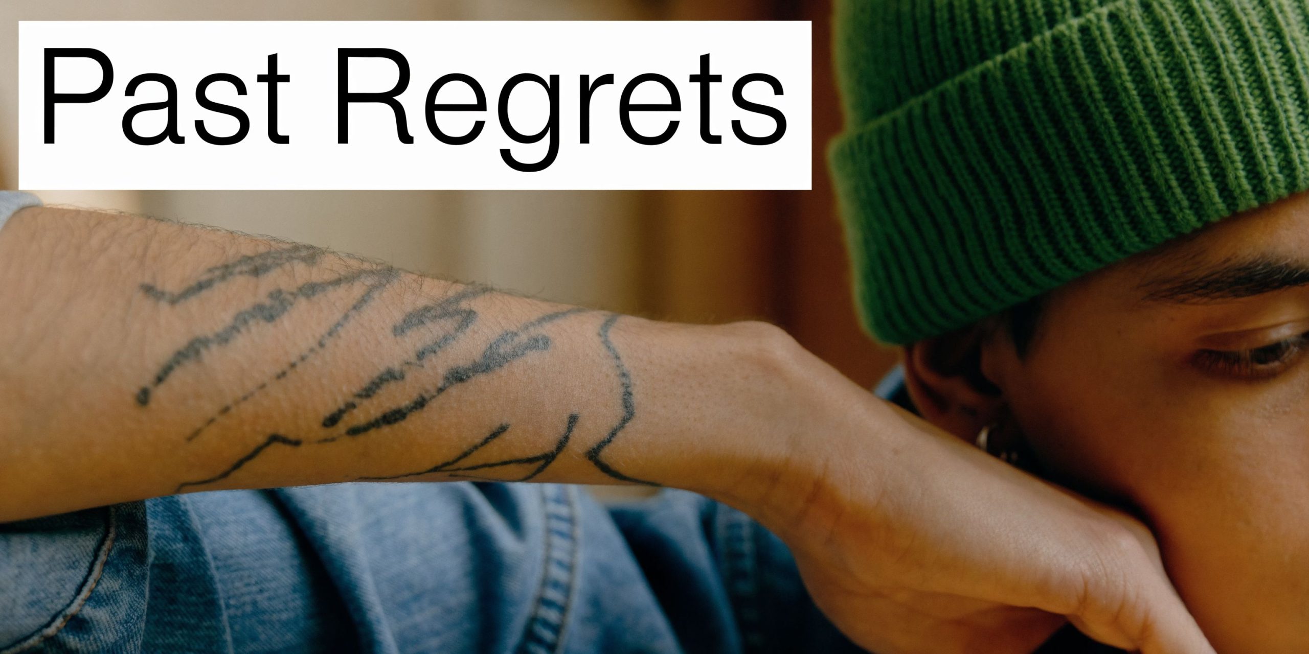 A close-up of a person with a green beanie looking down at their stick and poke tattoo.