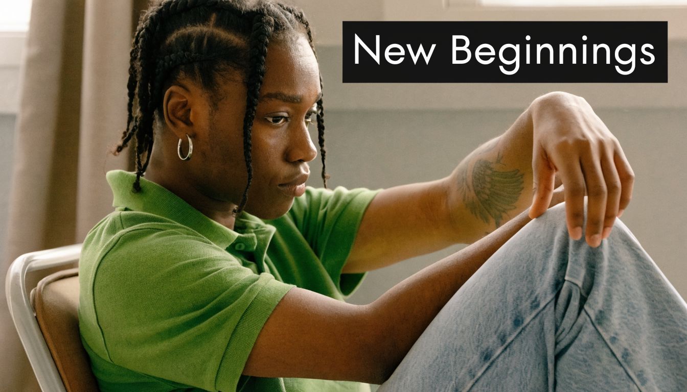 A young person with braided hair and a visible tattoo sitting thoughtfully on a chair.