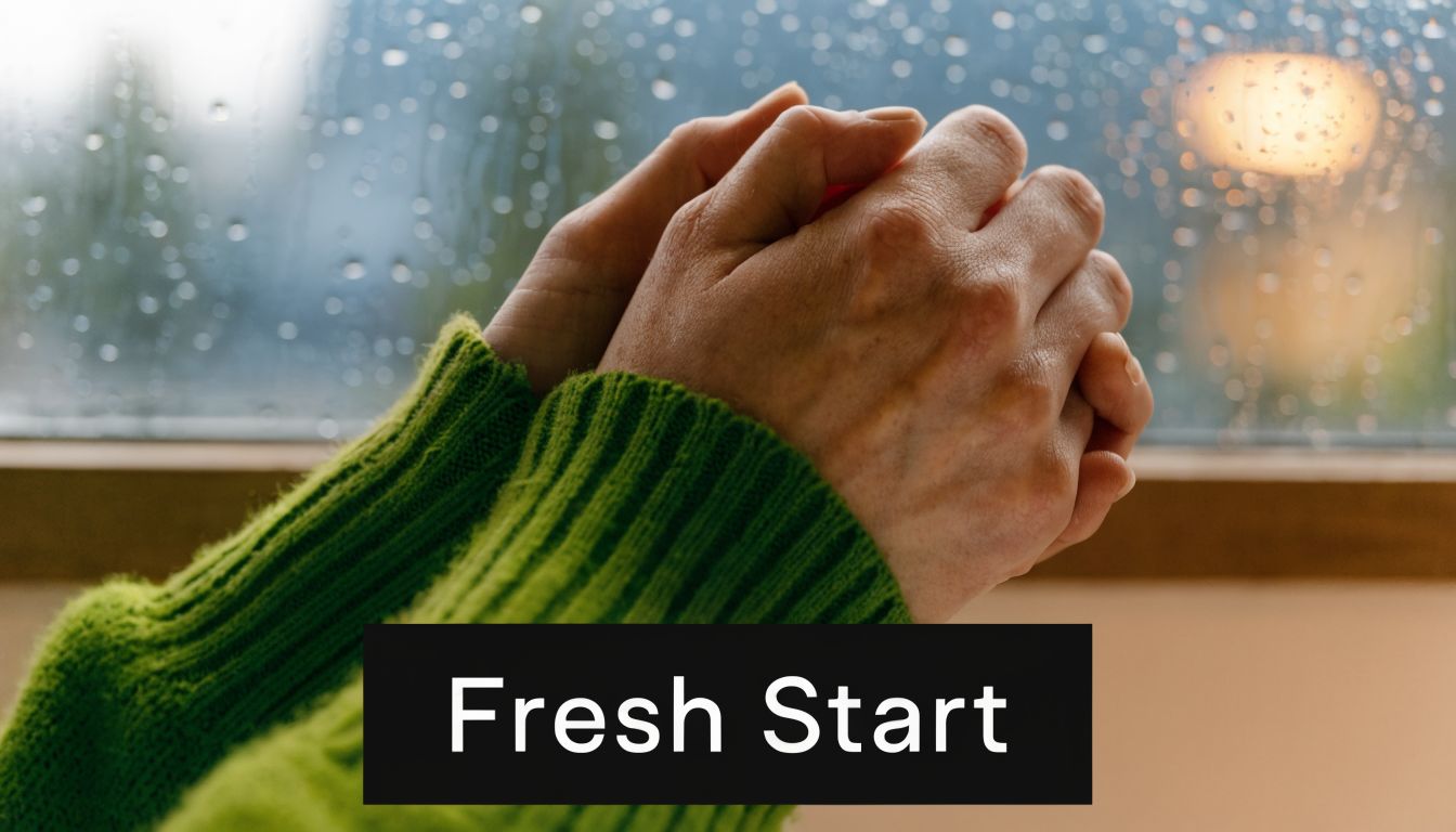 Close-up of hands clasped together with a green sweater against a rainy window backdrop.