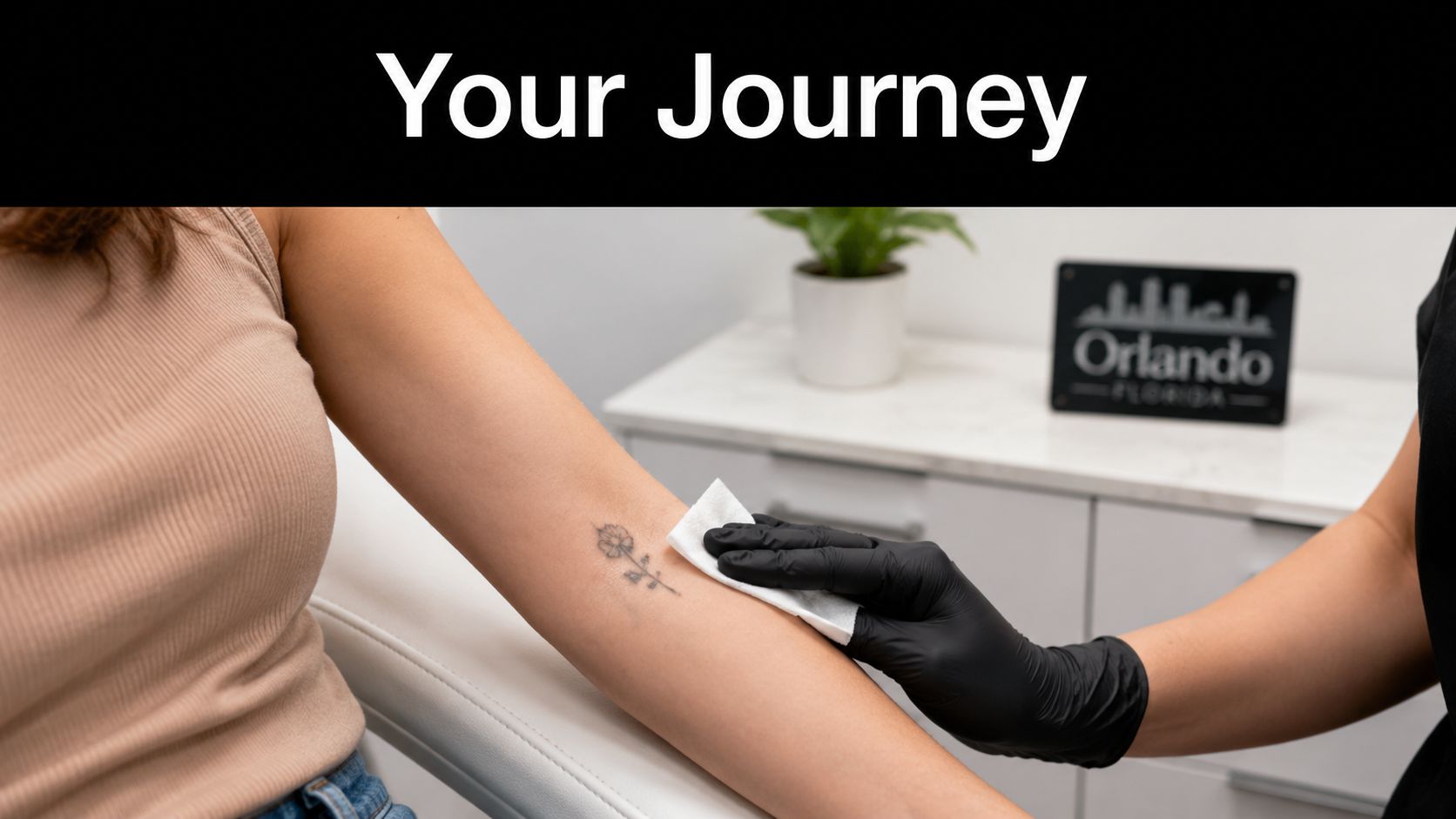 A professional technician wearing black gloves cleans a small flower tattoo on a client's arm with a wipe.