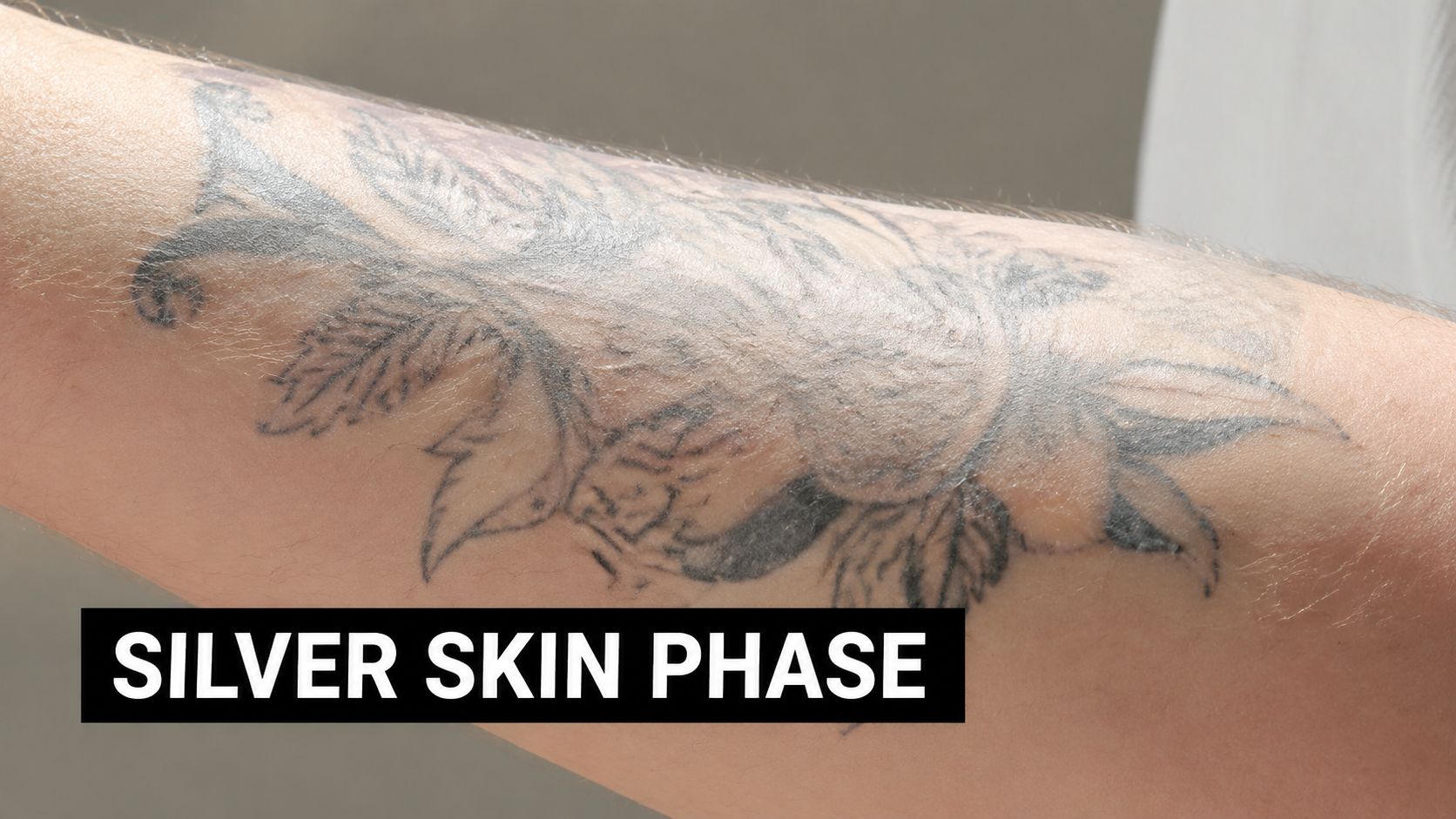 Close-up of a healing tattoo on an arm showing the characteristic shiny silver skin phase appearance.