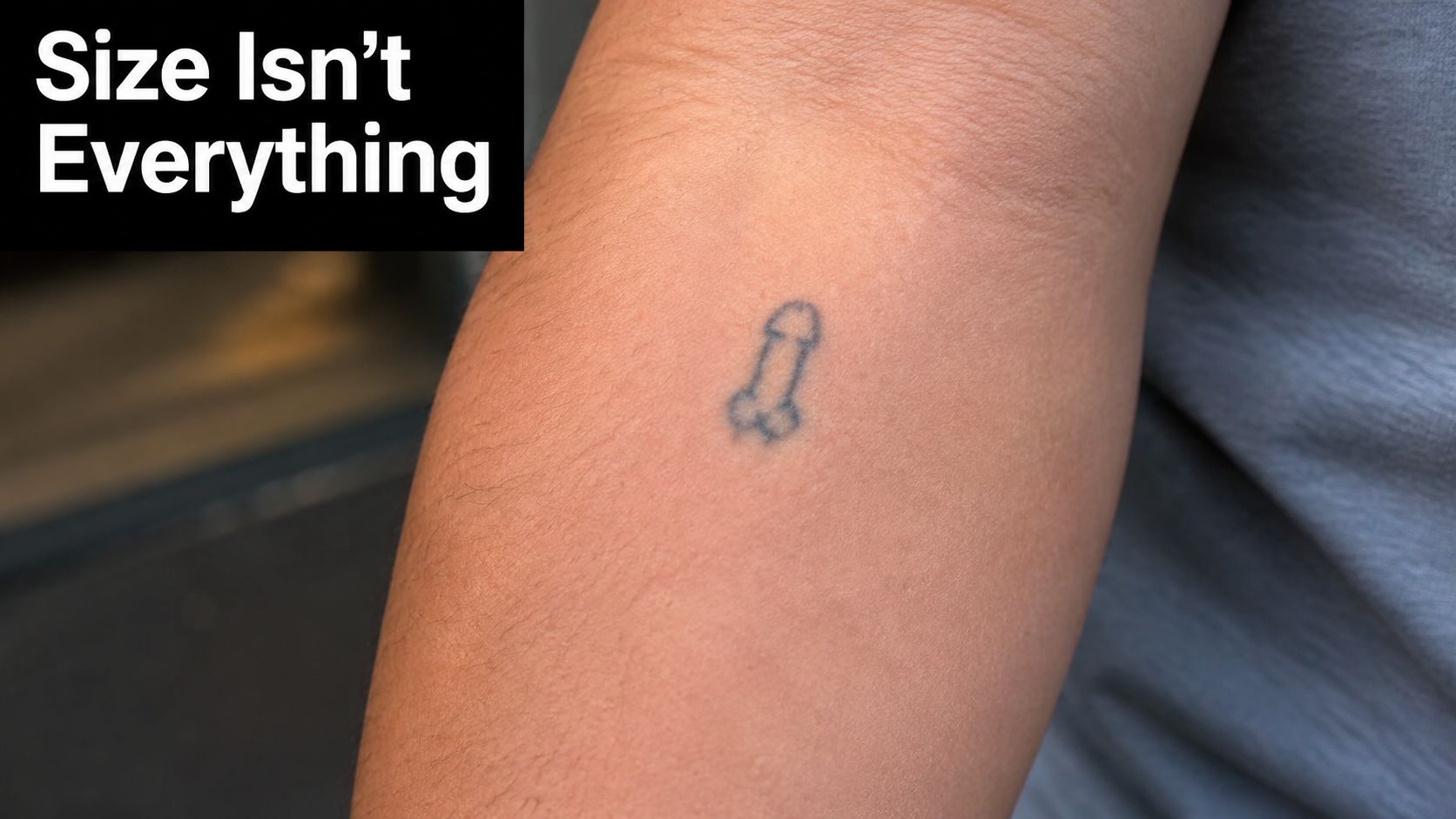 A close-up view of a person's forearm showing a tiny phallic-shaped tattoo with text overlaying the image.